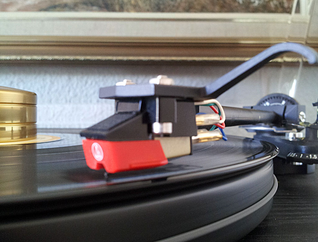 Close-up of a turntable with its cartridge and diamond stylus visible on the tonearm.
